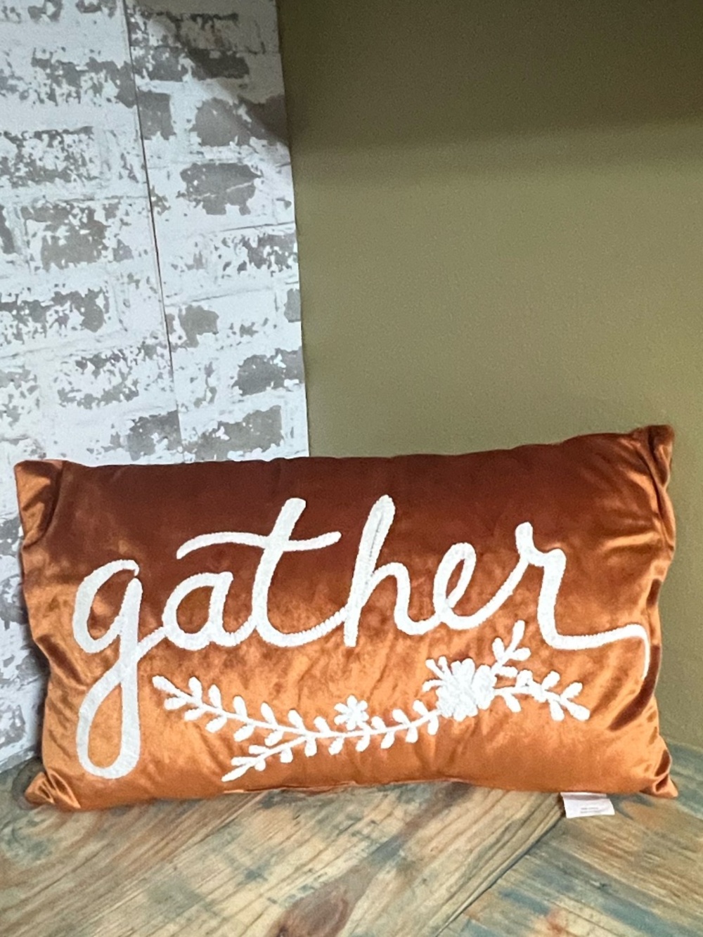 Rust-orange velvet lumbar accent pillow featuring white embroidered "gather"